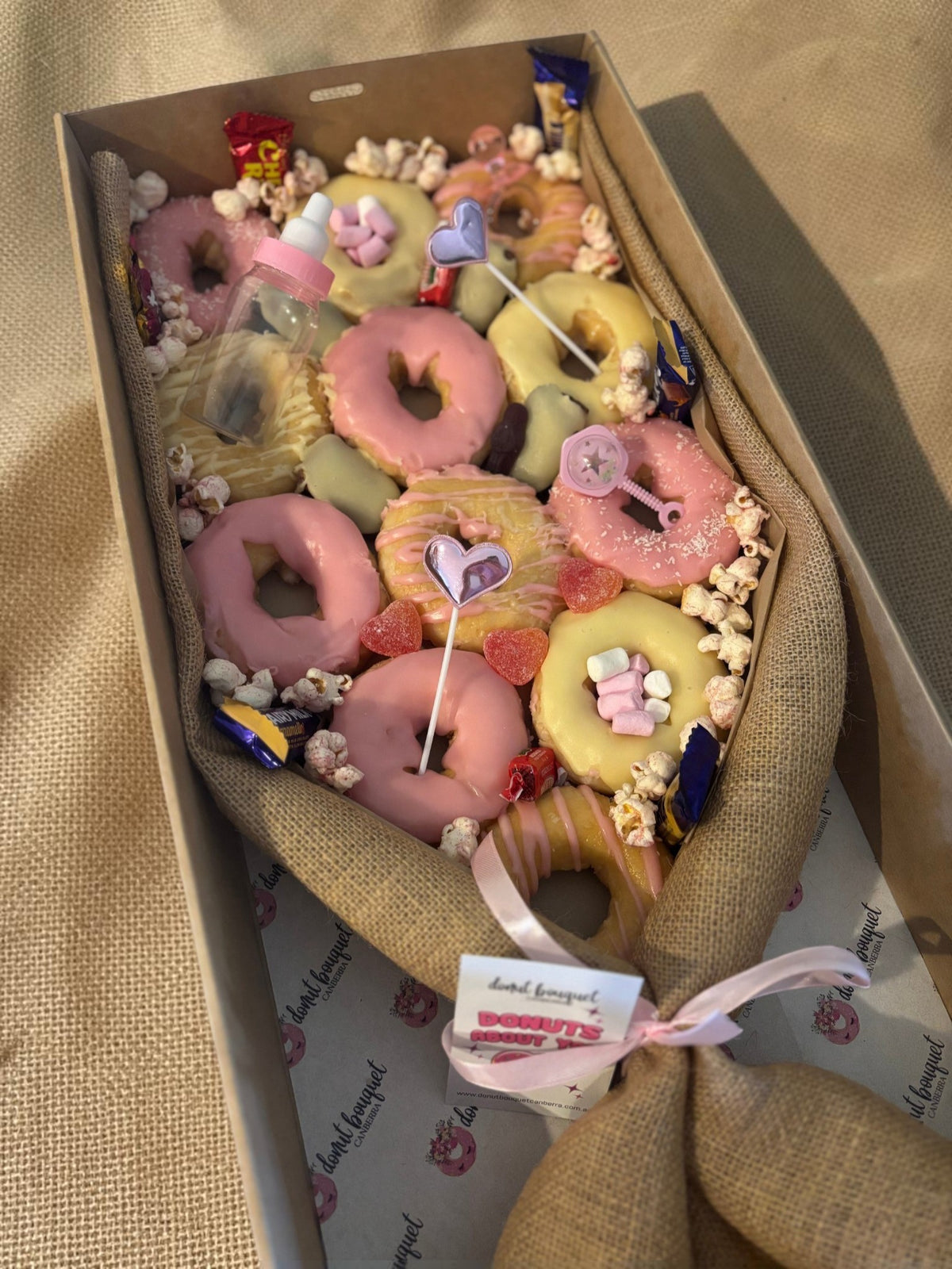 Donut Bouquet Canberra gluten free baby girl gift box featuring pink and yellow iced donuts with candy decorations.