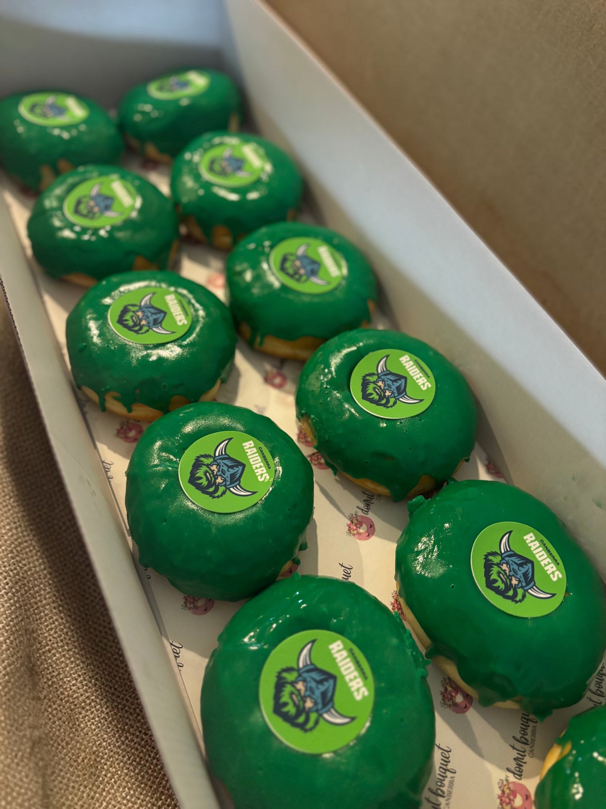 Donut Bouquet Canberra green glazed donuts arranged in rows inside cardboard boxes for a Raiders themed celebration.