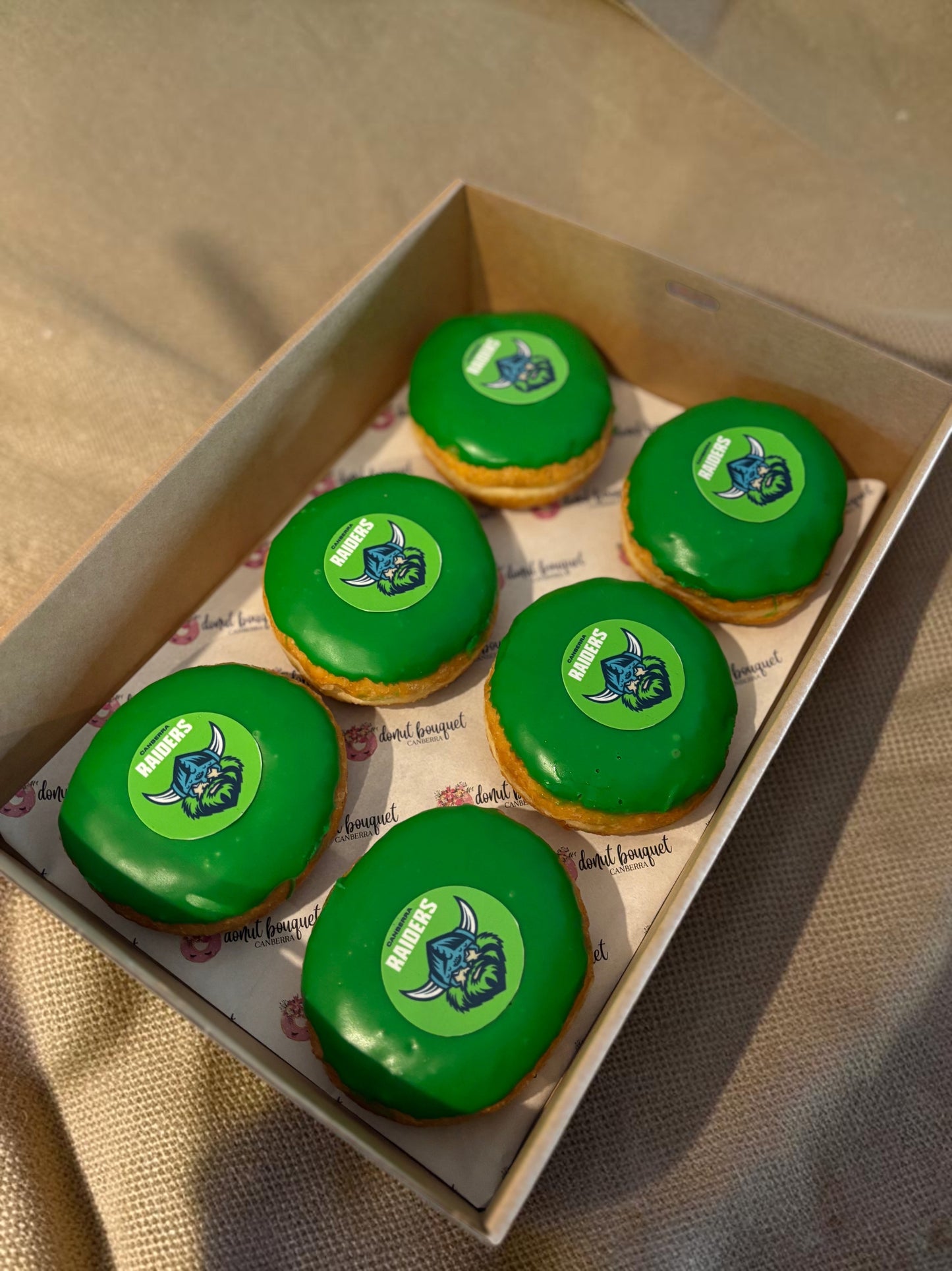 Donut Bouquet Canberra green glazed donuts arranged in rows inside cardboard boxes for a Raiders themed celebration.