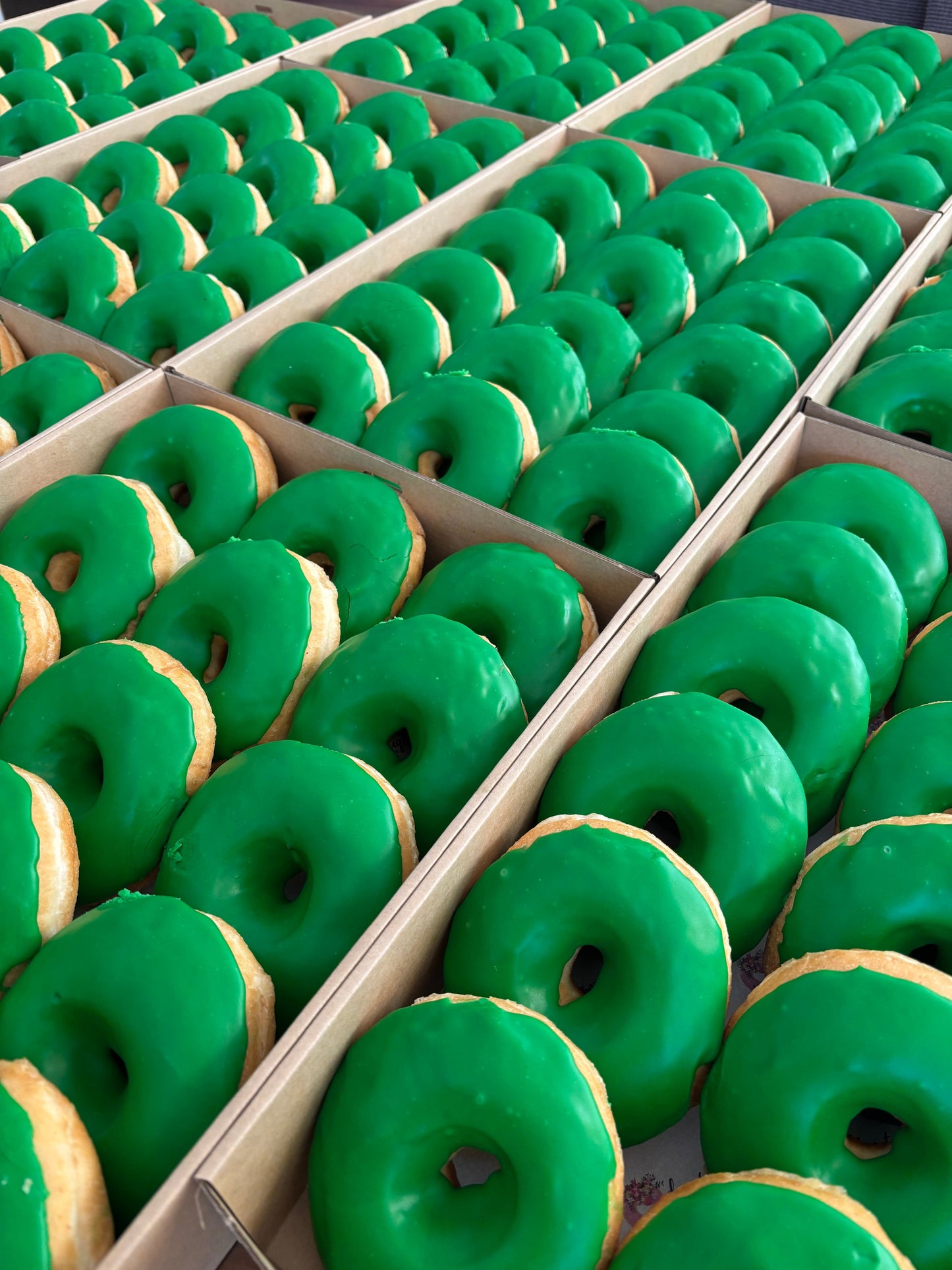 Donut Bouquet Canberra green glazed donuts arranged in rows inside cardboard boxes for a Raiders themed celebration.