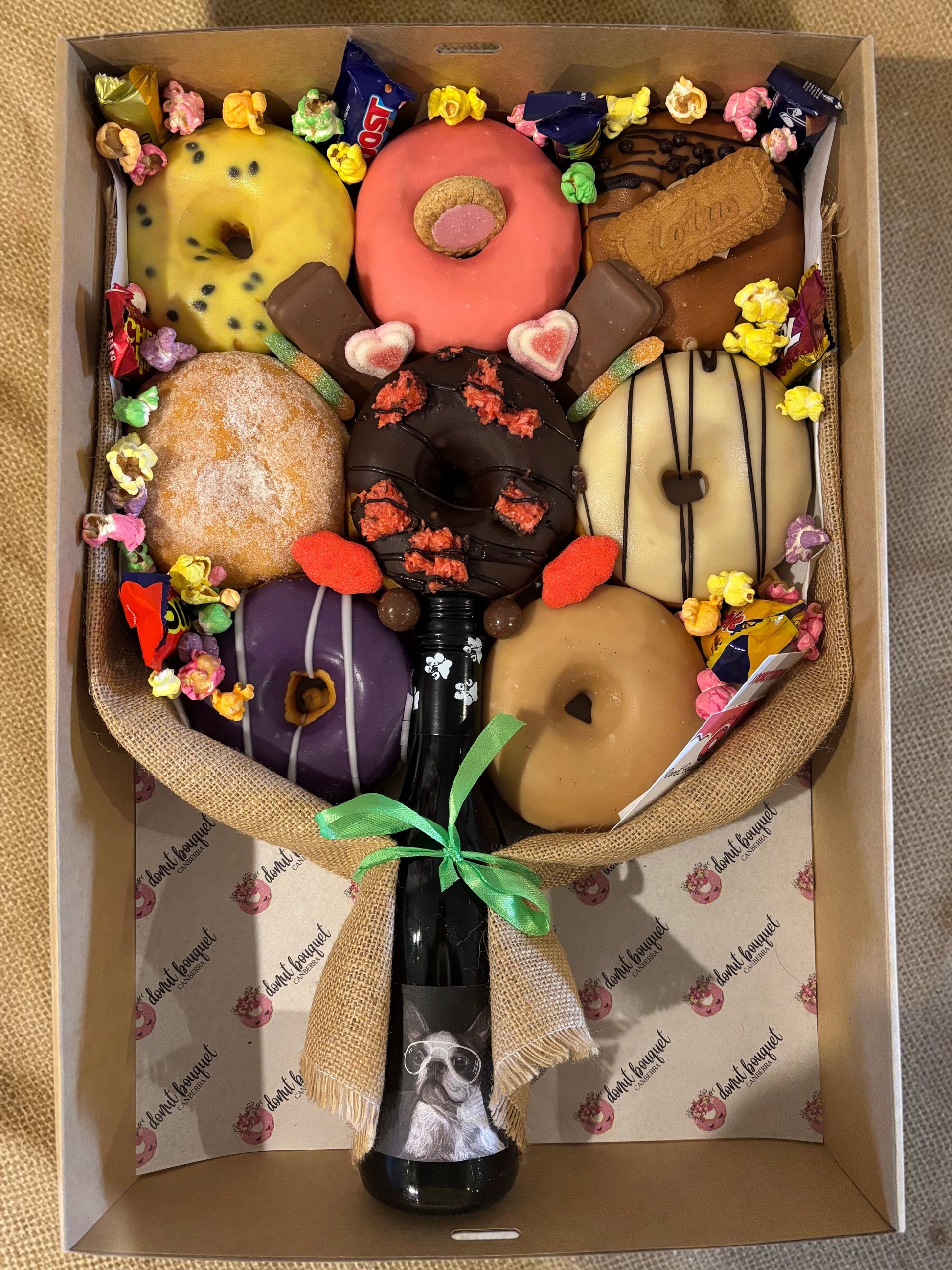 Donut Bouquet Canberra gift hamper featuring eight assorted glazed donuts, chocolates, and a central bottle of wine.